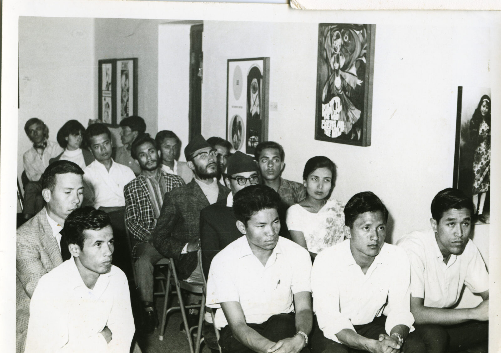 black and white photo of a group of people sitting in chairs in a gallery