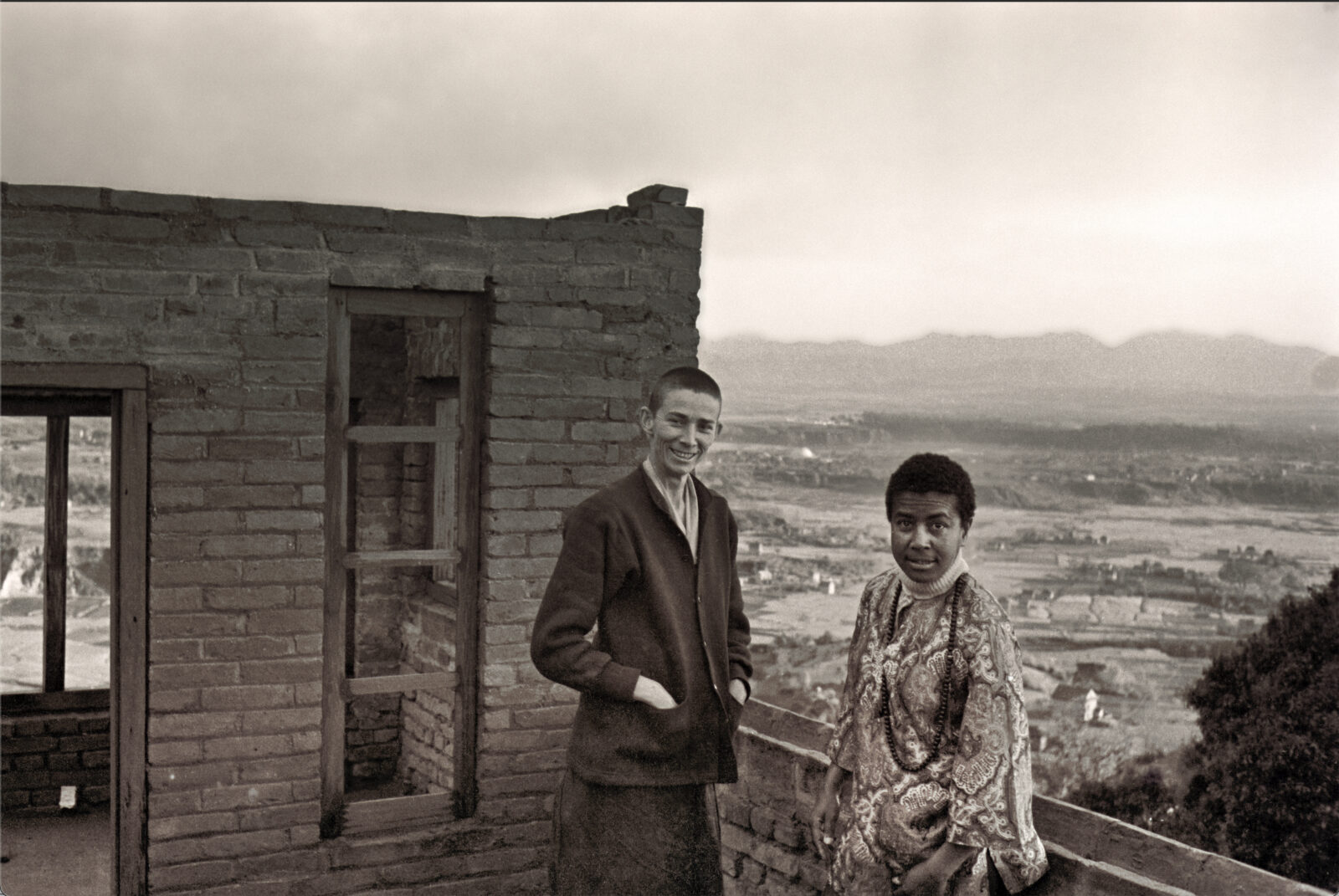 black and white photo of sister max and a friend standing on top of a building that overlooks kathmandu