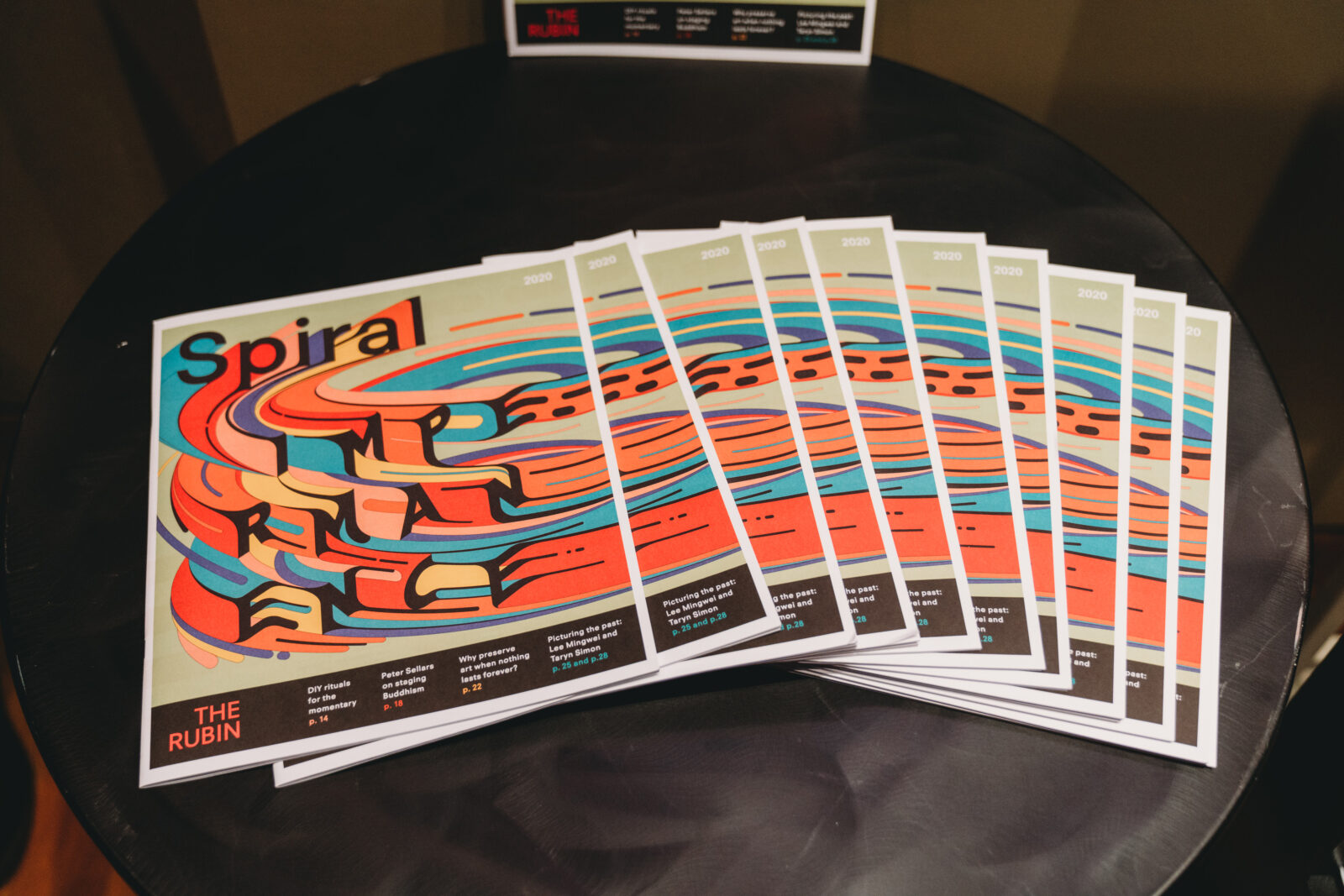 a stack of magazines fanned out on a black table with "Spiral IMPERMANENCE" on the cover