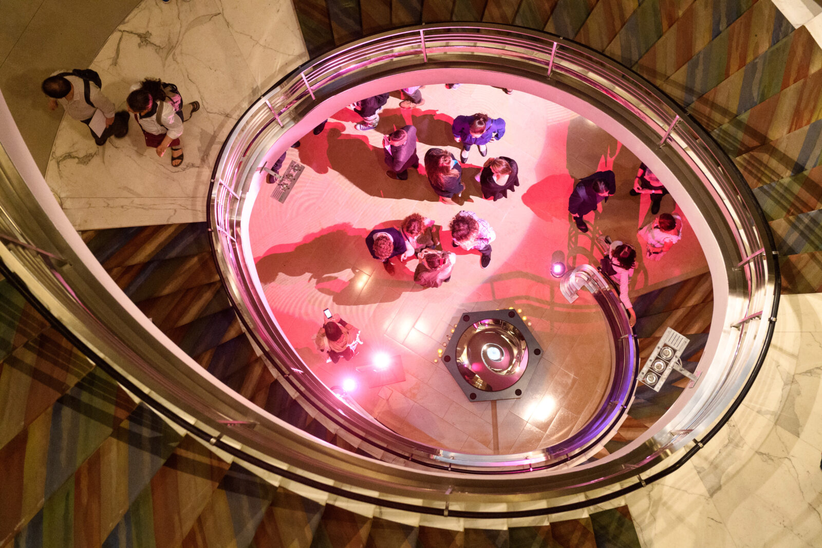 people stand together at the base of a spiral staircase while two people walk up the stairs