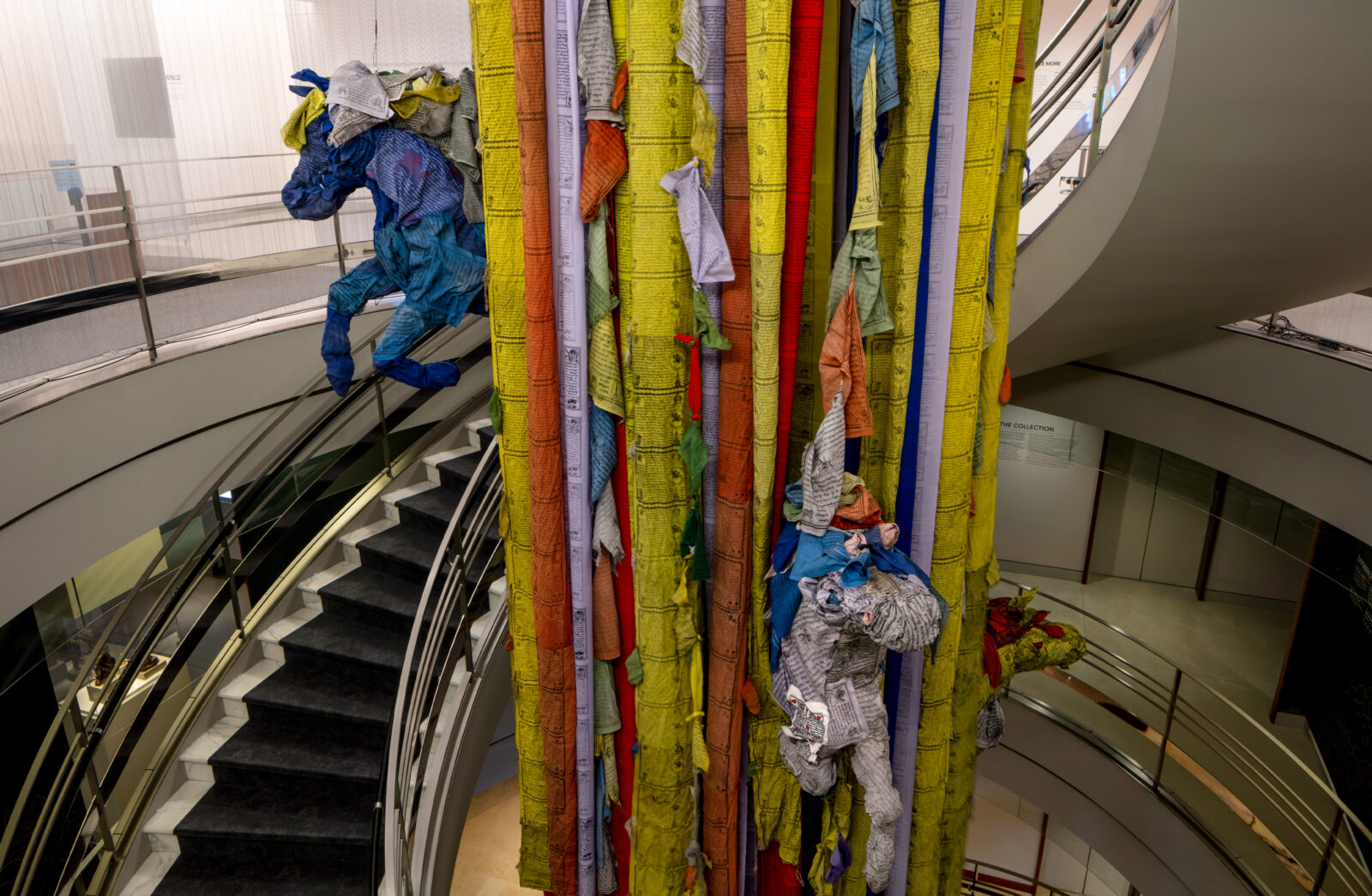 Prayer flags cascading down the center of a spiral staircase with sculpted horses come out from within the flags.