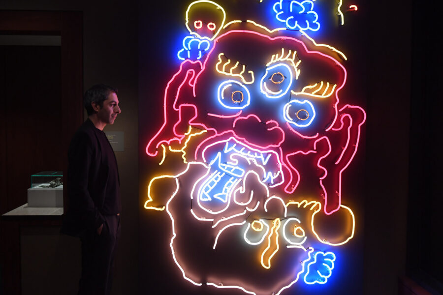 an adult man standing in profile while looking at a neon sculpture of two wrathful deities